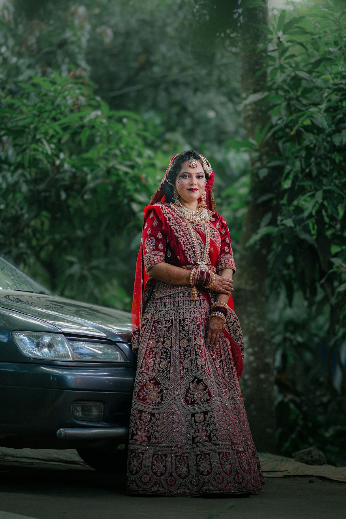 Bride in traditional red lehenga stands by car