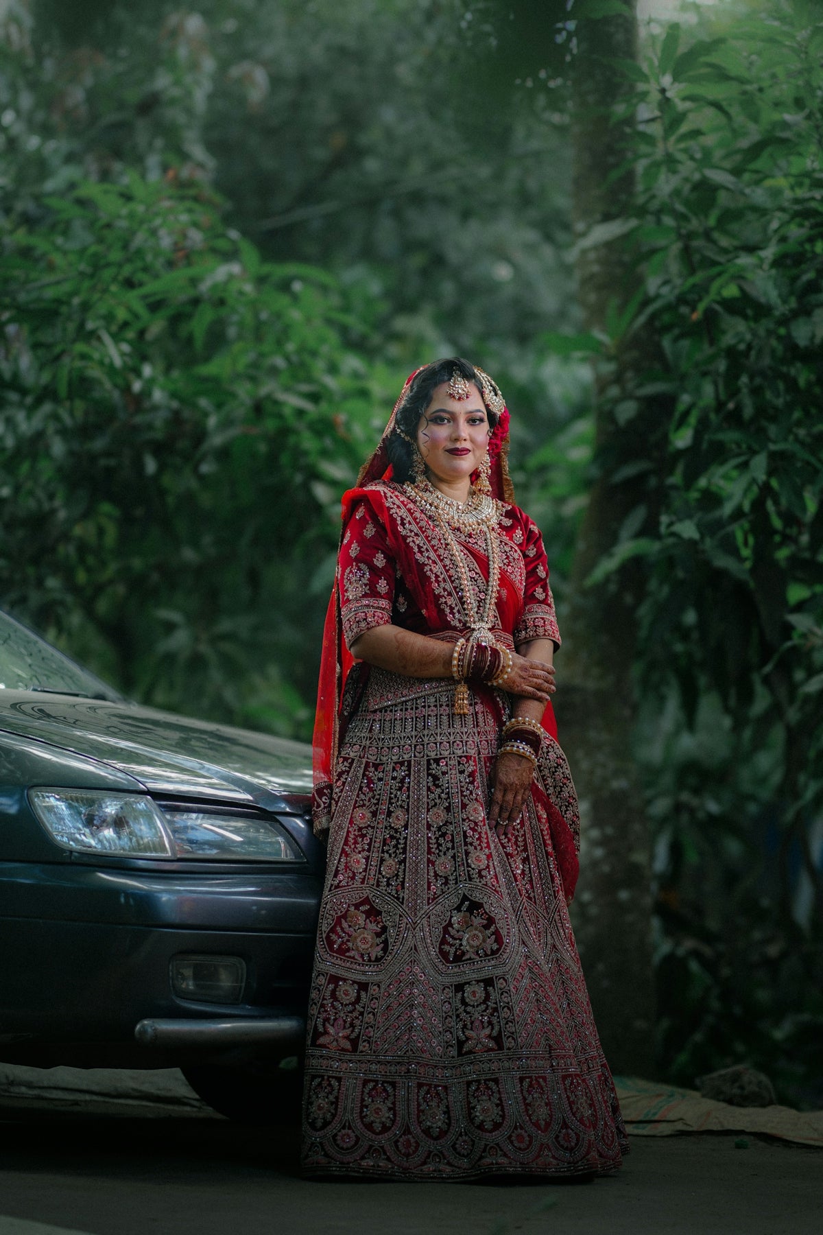 Bride in red lehenga standing next to car