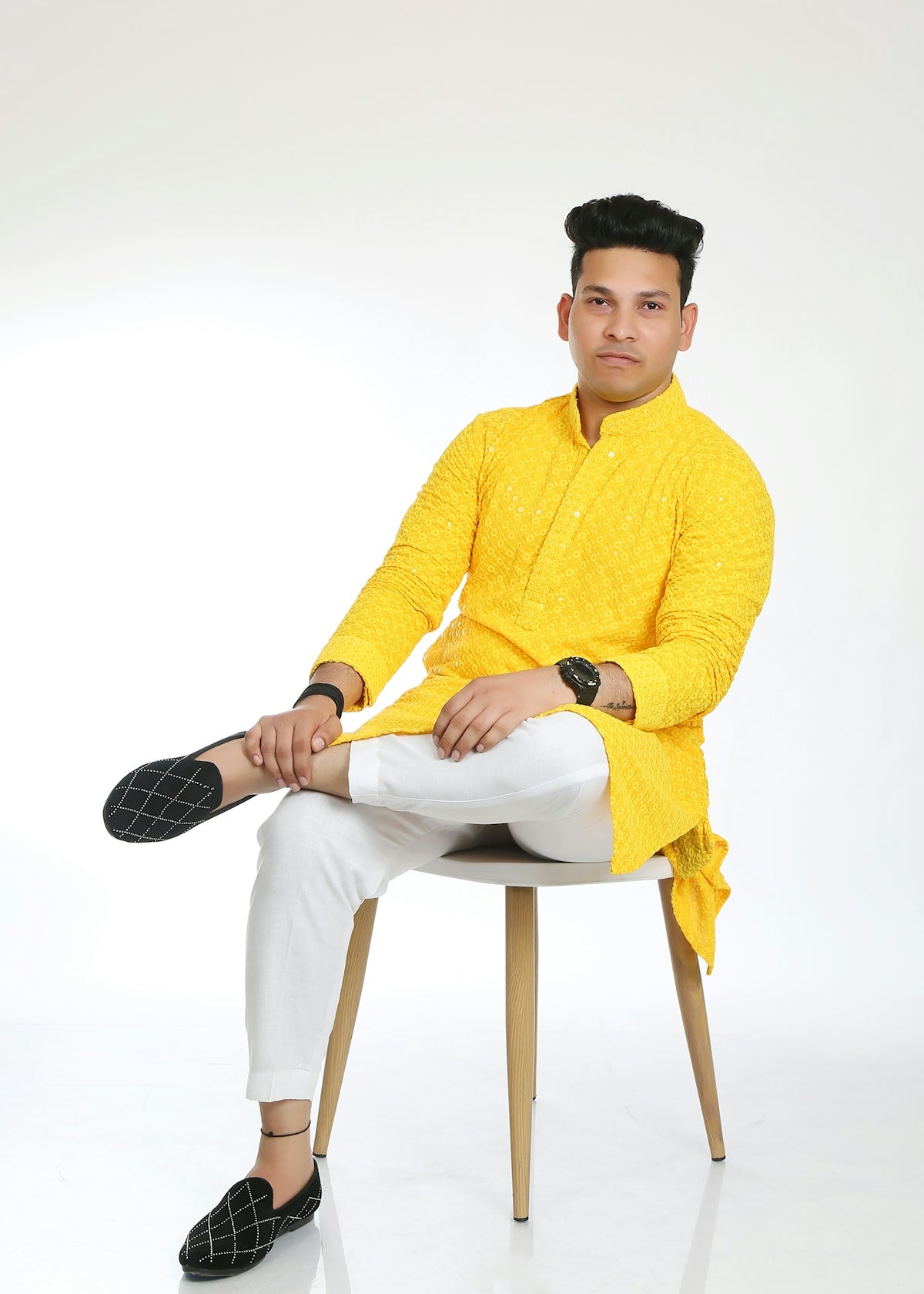 A man in a yellow kurta and white pants sits.