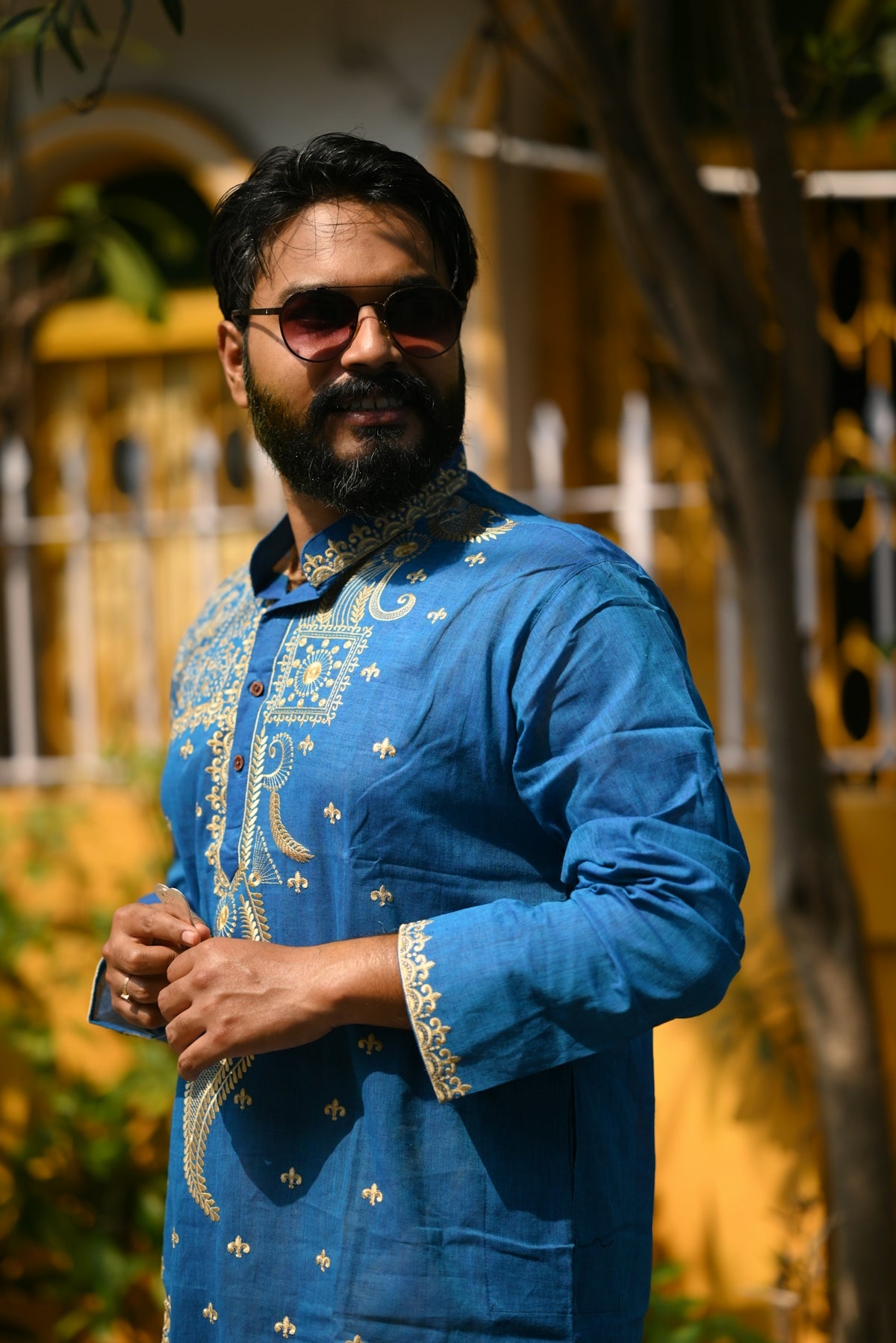 Man in blue kurta with sunglasses poses outdoors.