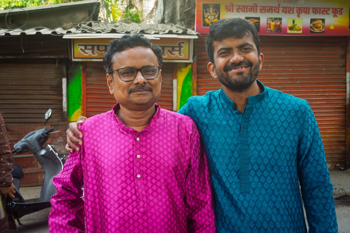 Two men in kurtas stand together outdoors.