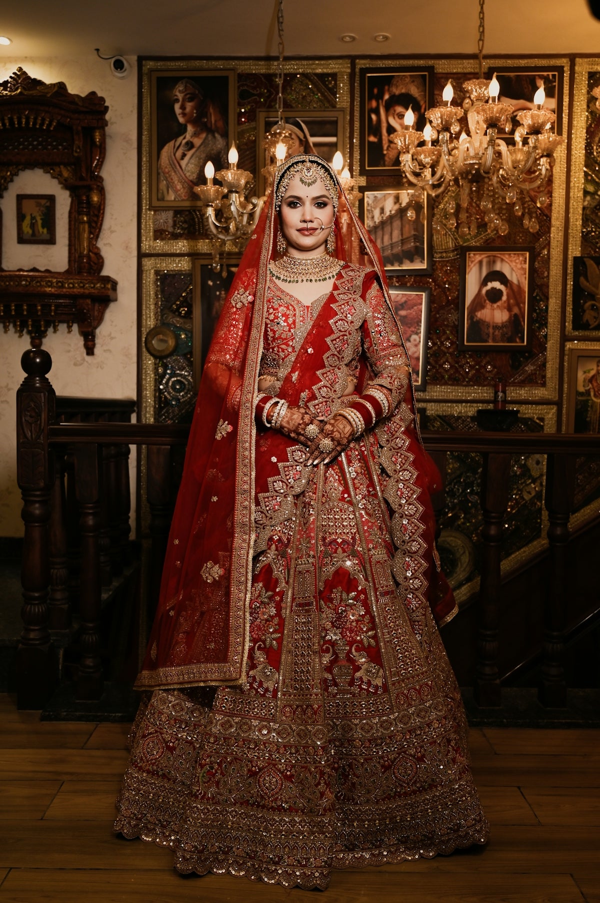 A woman in a red embroidered lehenga and veil standing in a decorated room
