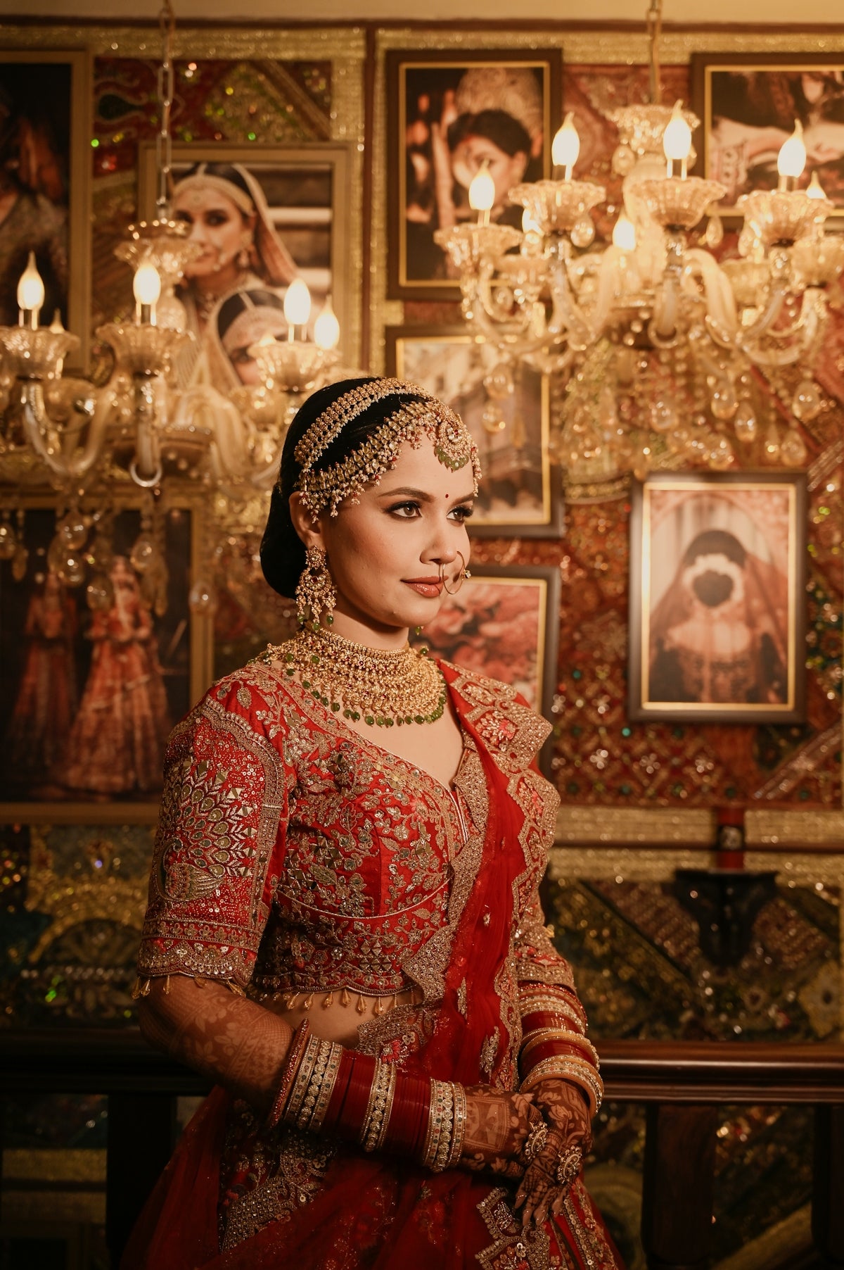 A woman in a red embroidered lehenga and traditional gold jewelry in a room